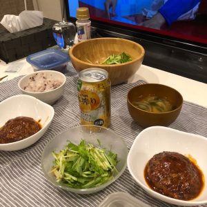 テーブルの上に2人分のハンバーグとサラダと缶チューハイが並んでいる写真の画像