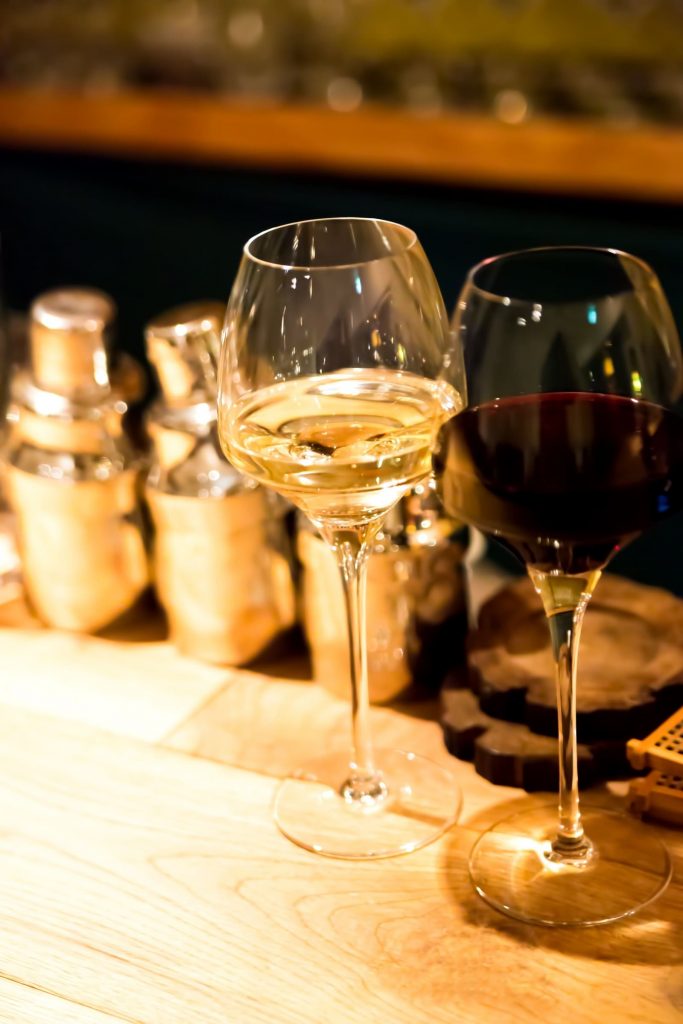 バーカウンターに並んだワイングラスに入った赤ワインと白ワインの写真の画像