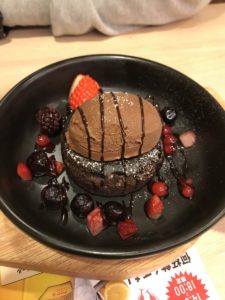 黒い器に盛られたチョコアイスとフルーツが乗ったチョコケーキの写真の画像