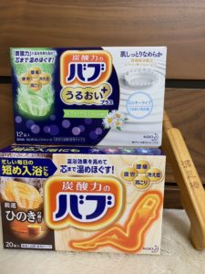 積まれた2種類の入浴剤の箱と一緒に置かれたツボ押し用のマッサージ棒の写真の画像