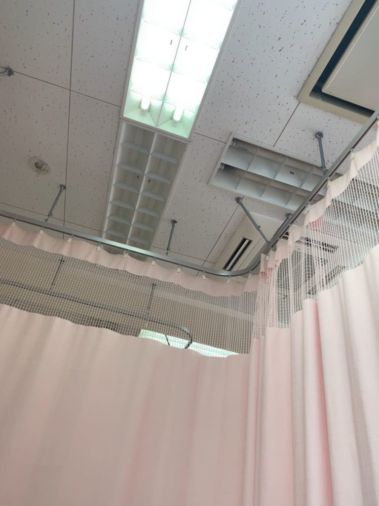 病院の天井と淡いピンクのカーテンの写真の画像
